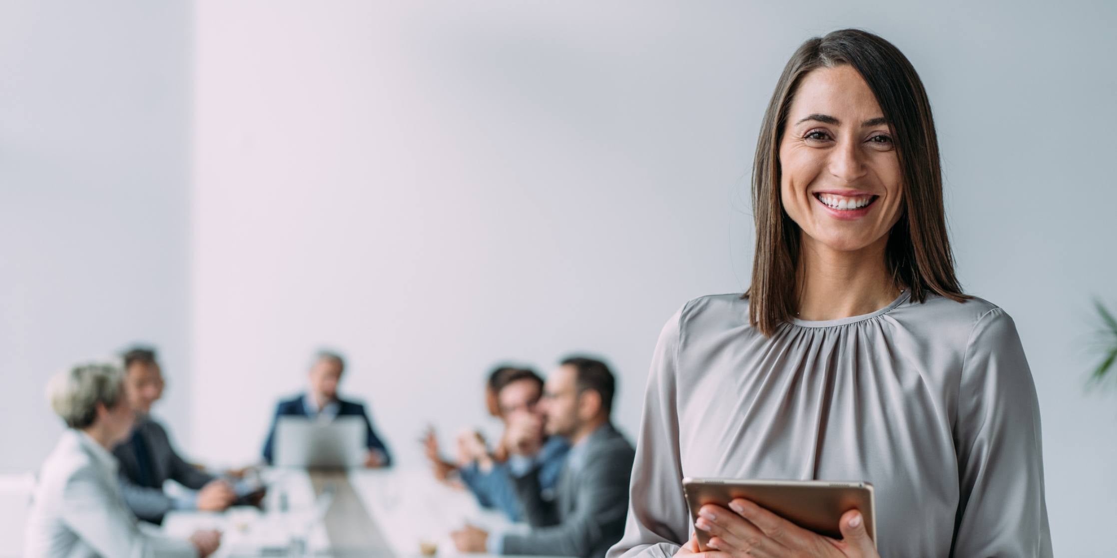 smiling businesswoman standing in front of her team and holding digital tablet