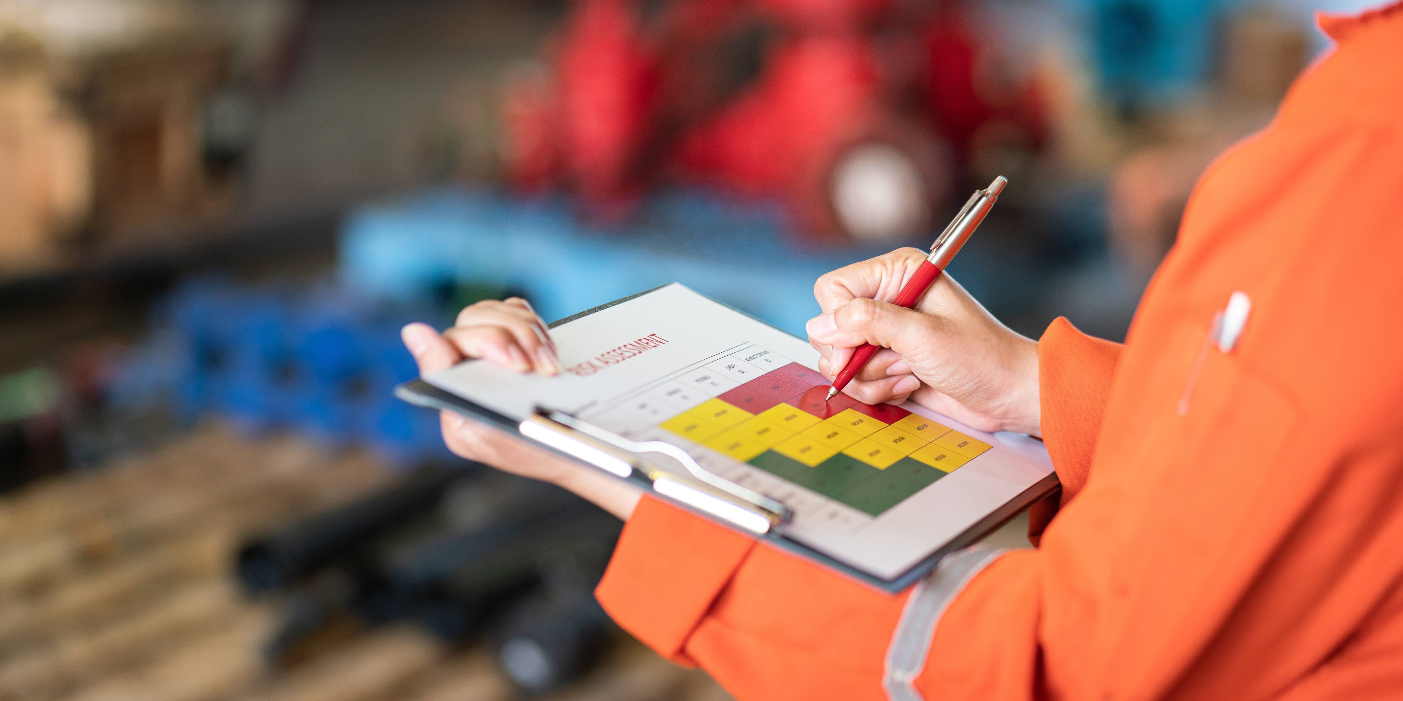 Person holding clipboard and writing with risk assessment on it