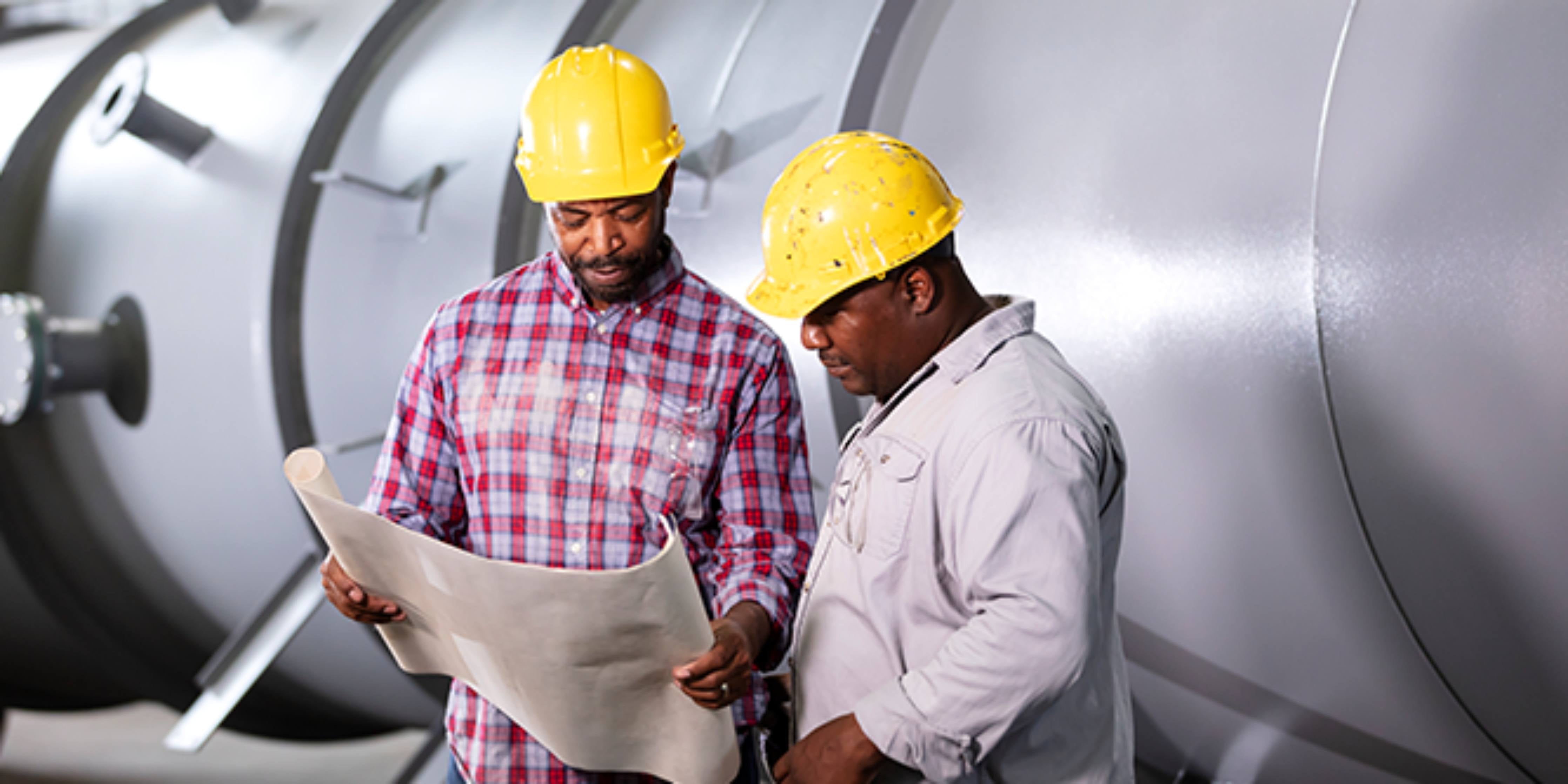 two workers wearing yellow hard hats holding paper