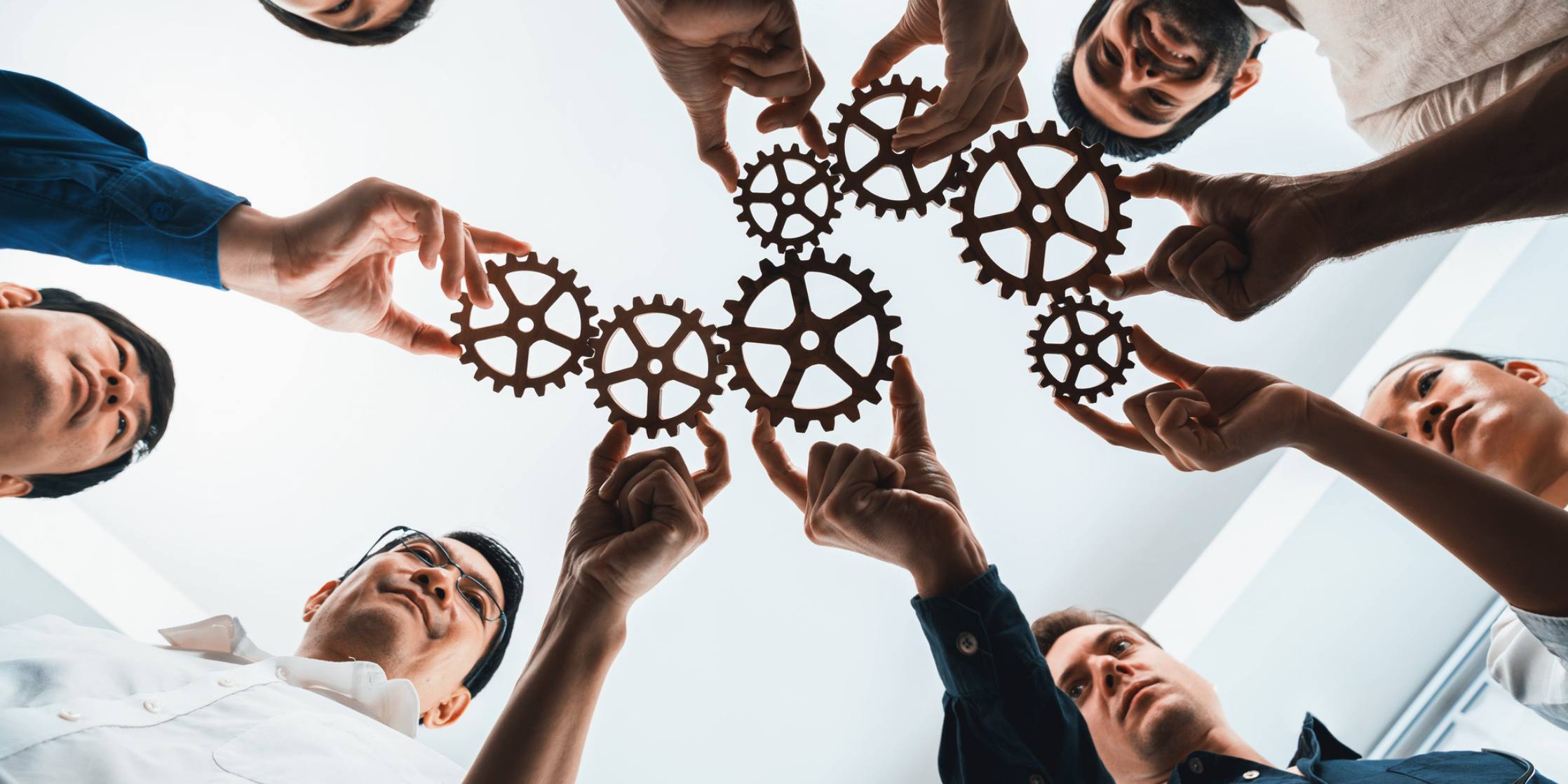 People holding interlocking gears together, symbolizing teamwork and collaboration.