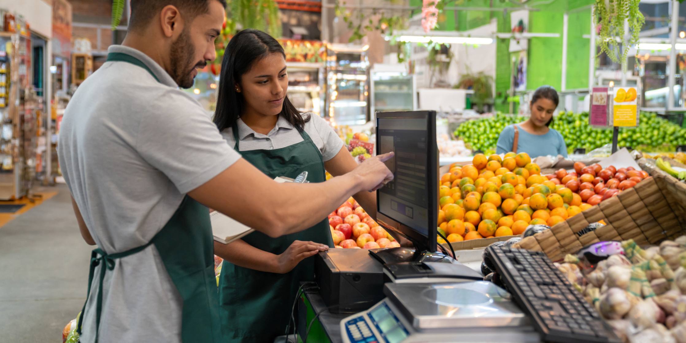 Business manager training a new employee at the supermarket and teaching her to work the cash register