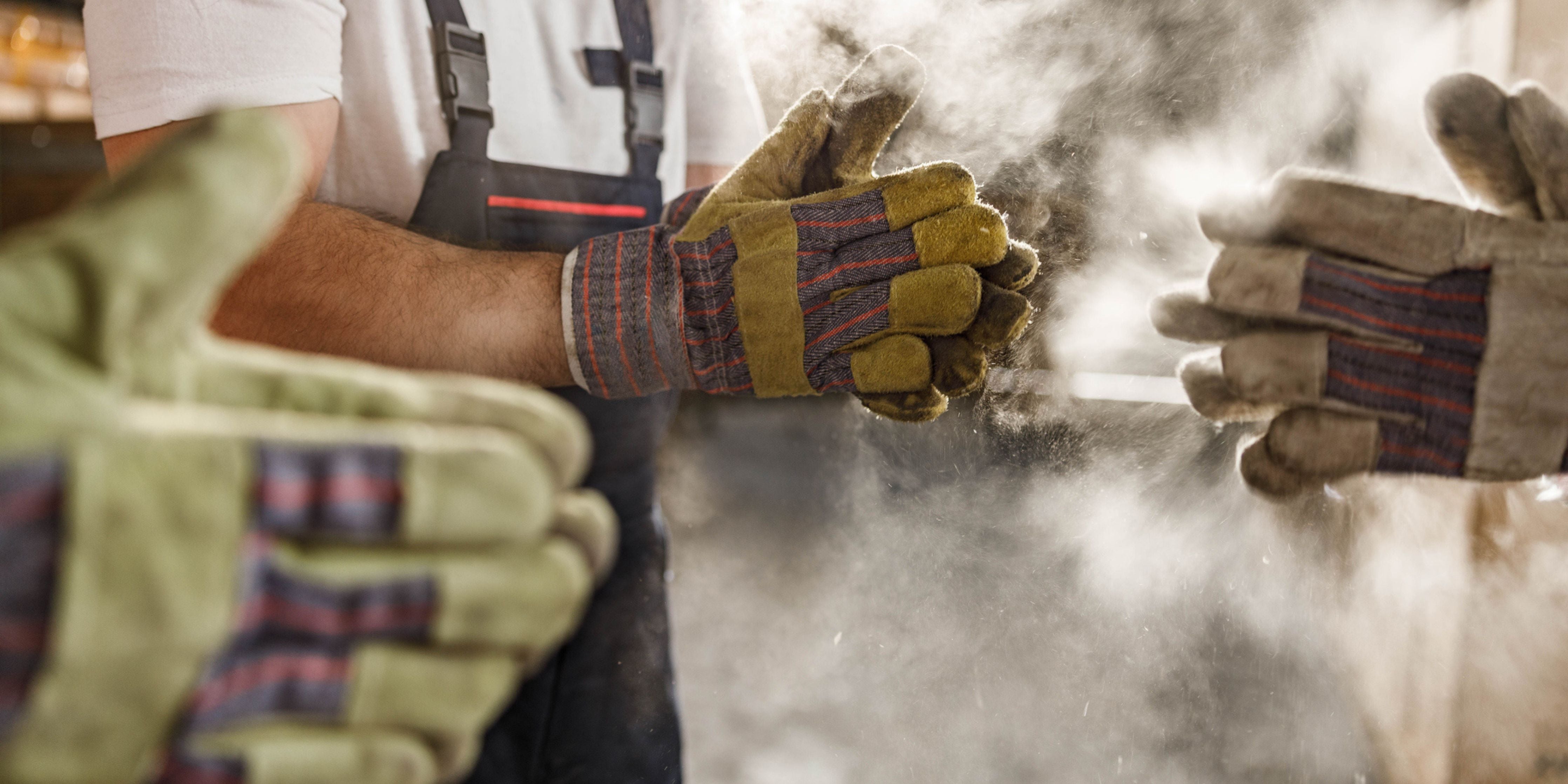 Close up of unrecognizable manual workers cleaning dust from their gloves in a factory.