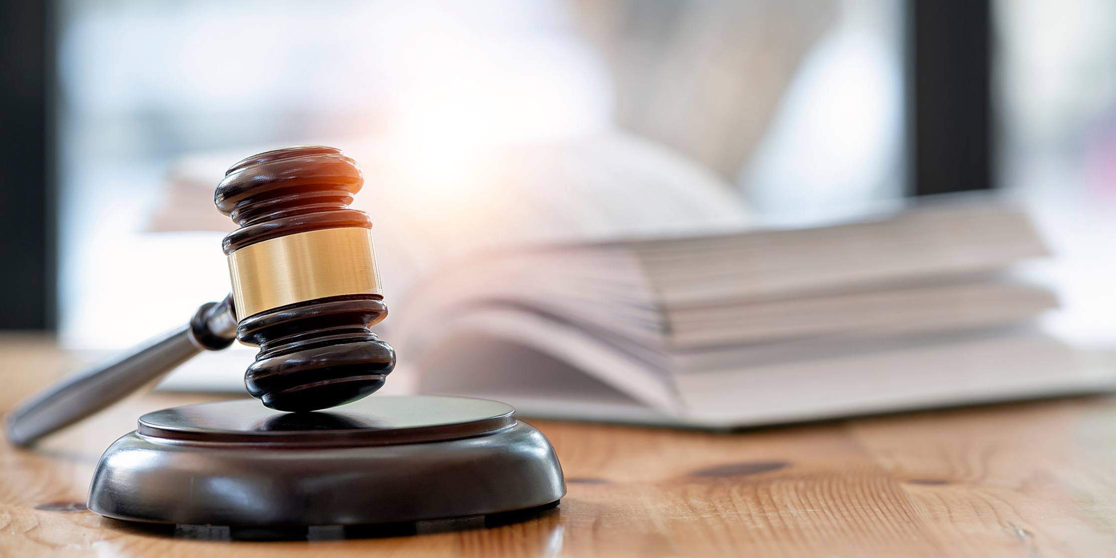 Wooden brown judge gavel on the table in the foreground, open book in the background