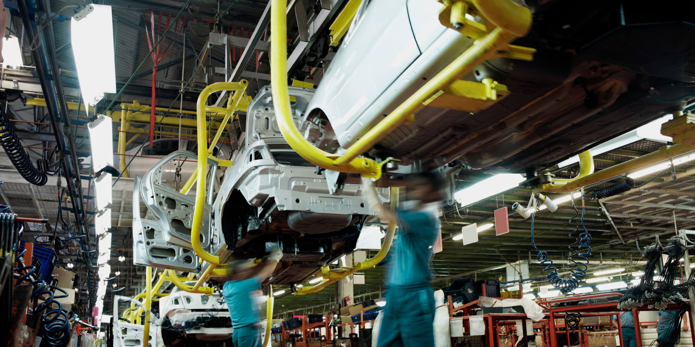 Automotive assembly line with a car being worked on by technicians in a factory setting.