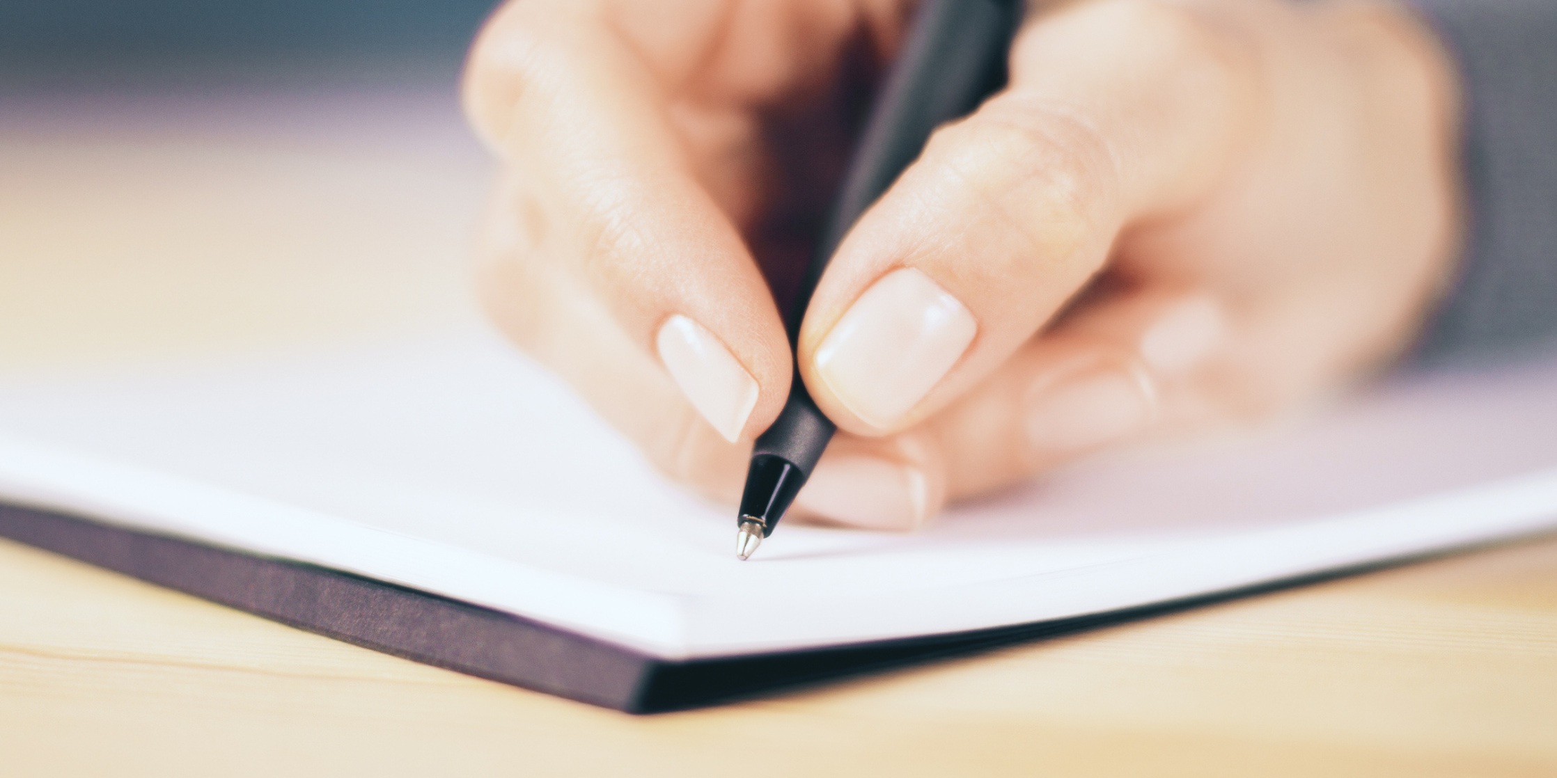 close up of a hand grasping a pen about to write on a note pad