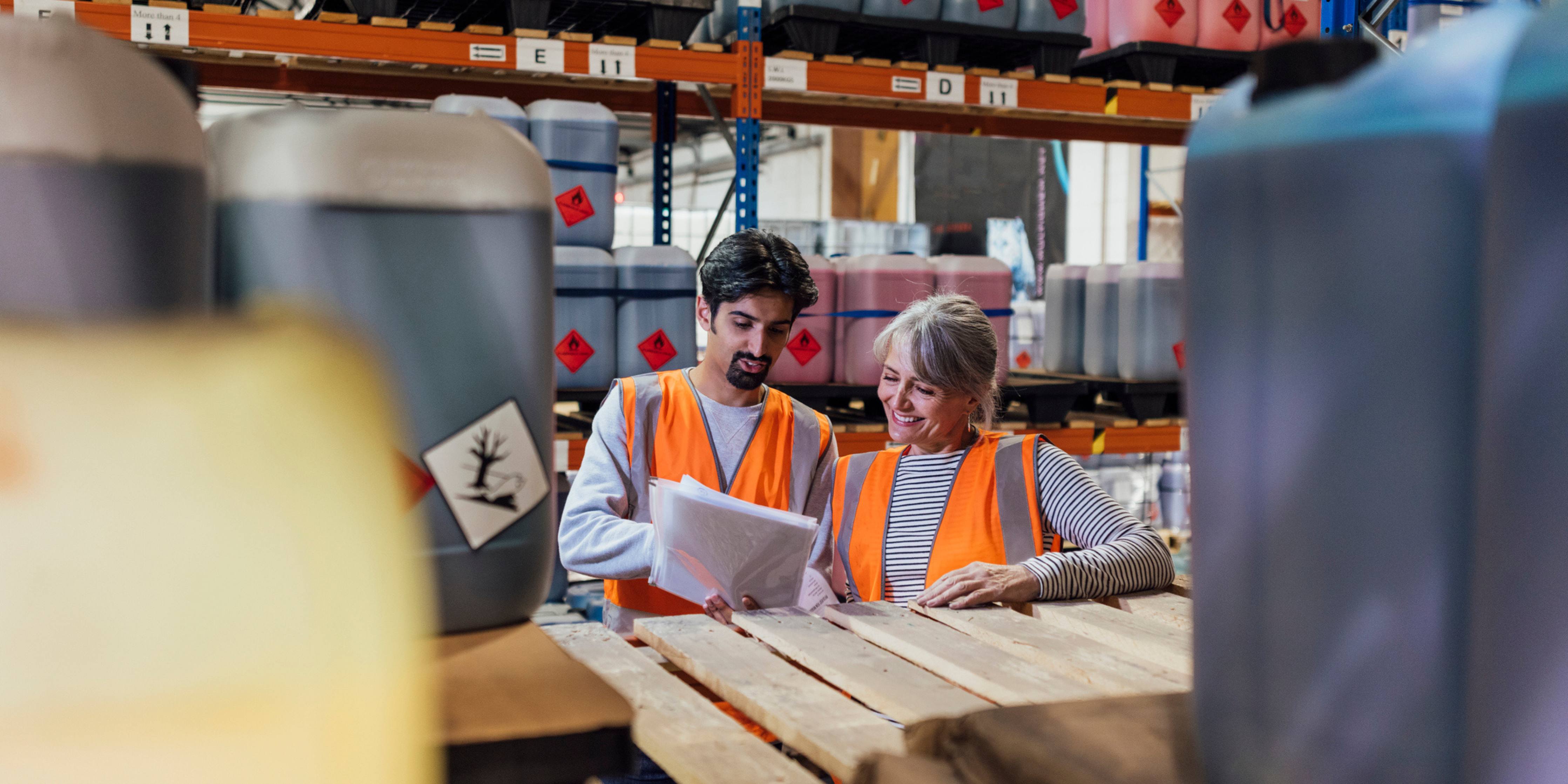 Image of two people wearing safety vests standing in a warehouse by a skid