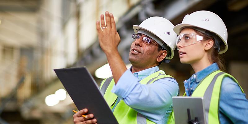 Image of two workers on a work site wearing safety hat, glasses and vest