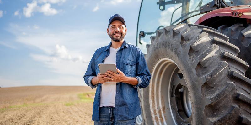 Portrait of farmer standing in front of a tractor holding a tablet