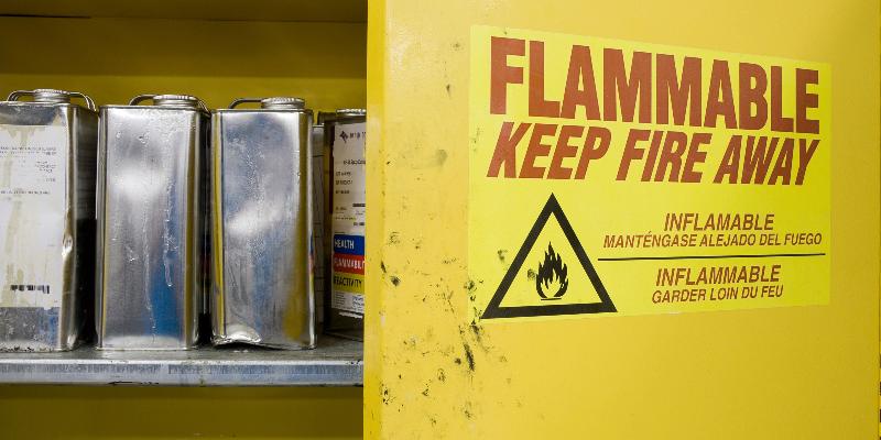 Open cabinet containing hazardous chemicals. Cans are dented and leaking with warning label visible.