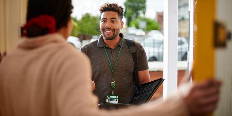 A friendly man wearing an id badge around his neck standing at the front door, speaking with the person who answered the door. 