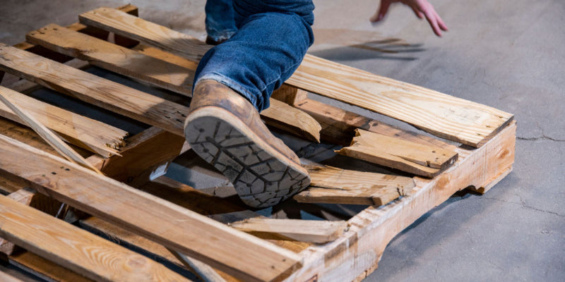  A close-up of a person stepping on a broken pallet that poses a severe risk of causing a fall and injury.