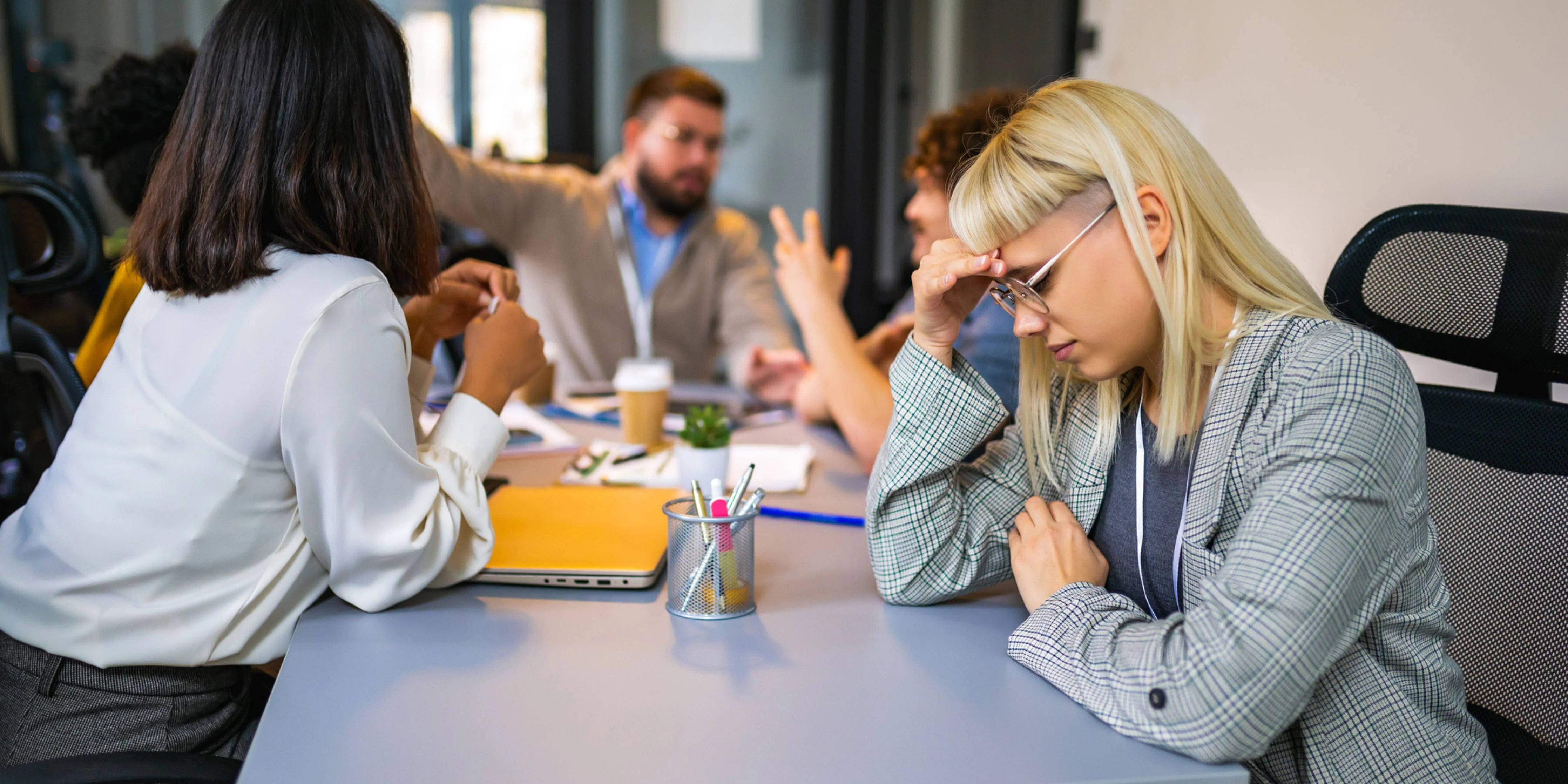 Image of a woman sitting with hand on forehead during a meeting