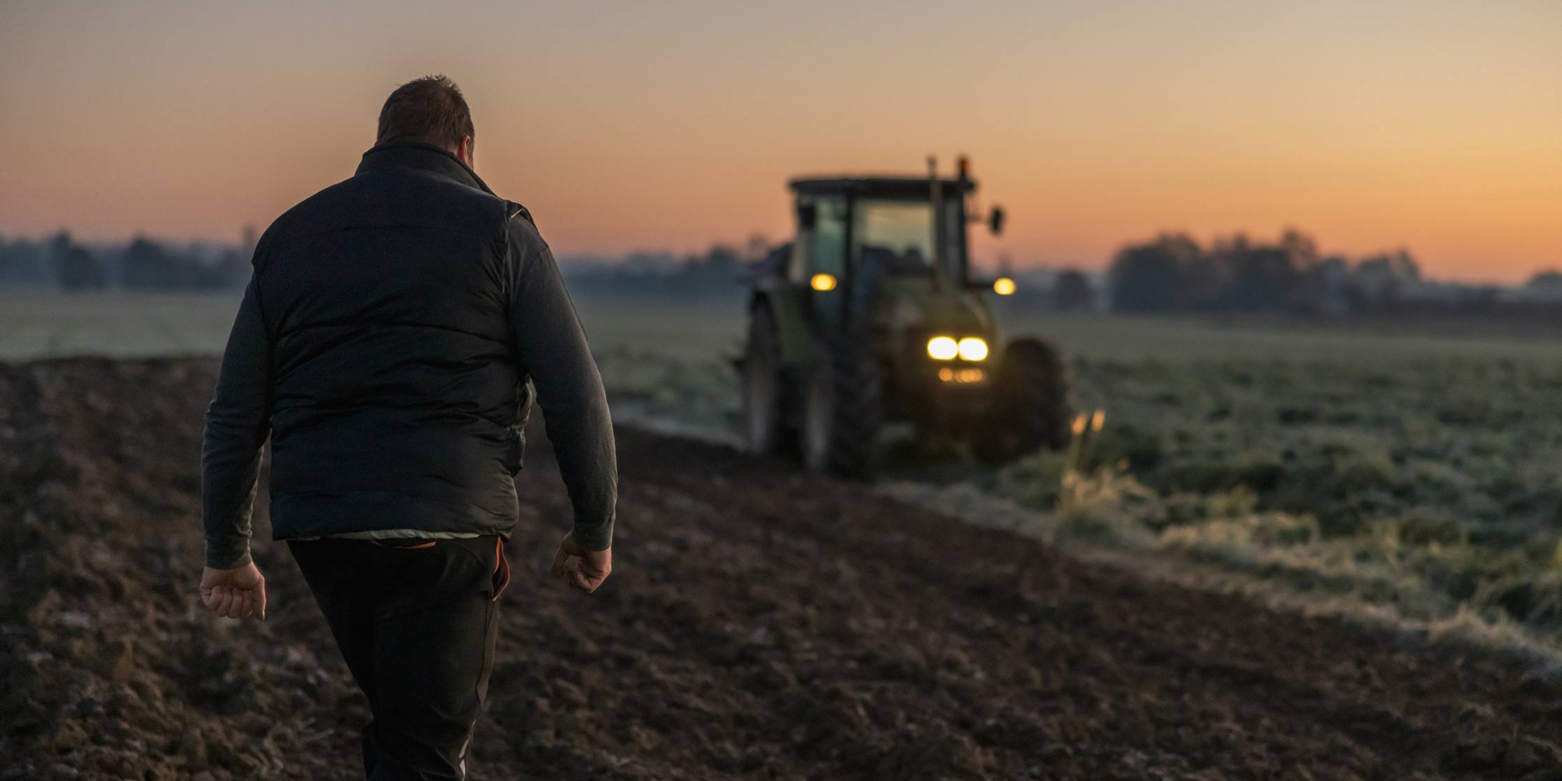 Man walking towards a tractor in a field at sunset