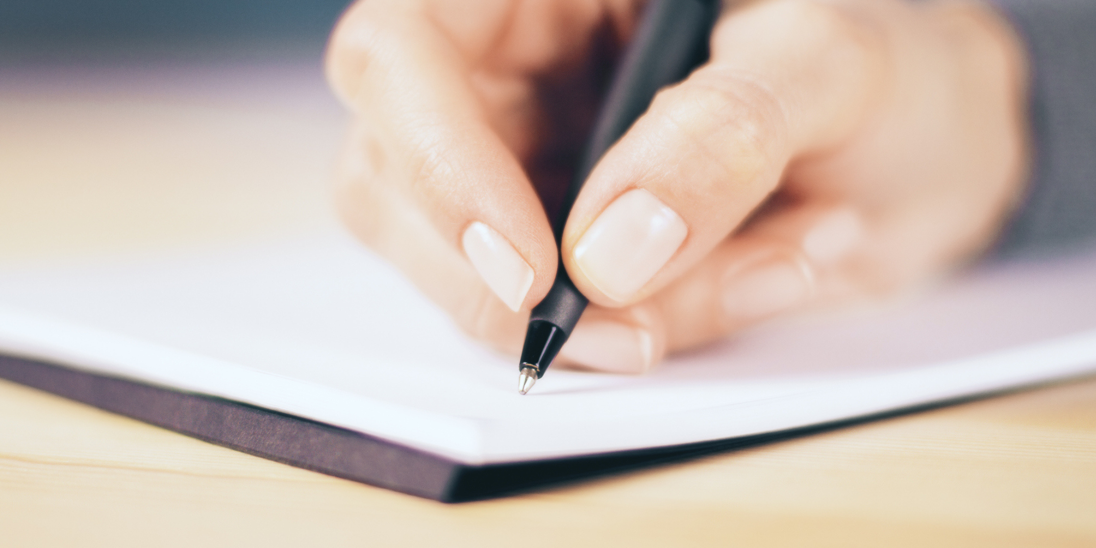 Close-up of hand writing with a pen on notebook