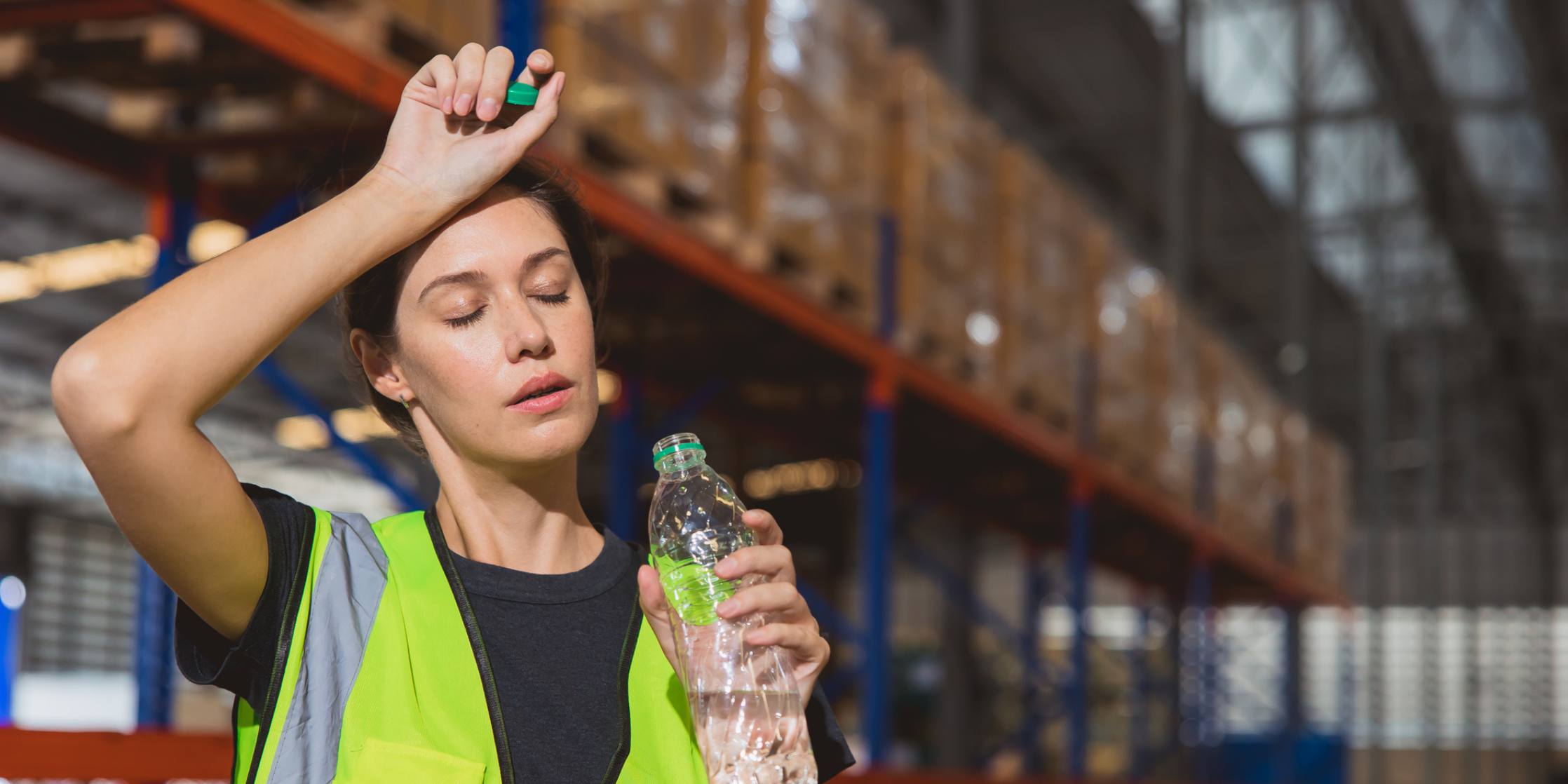 Person in a warehouse holding a water bottle, looking dehydrated