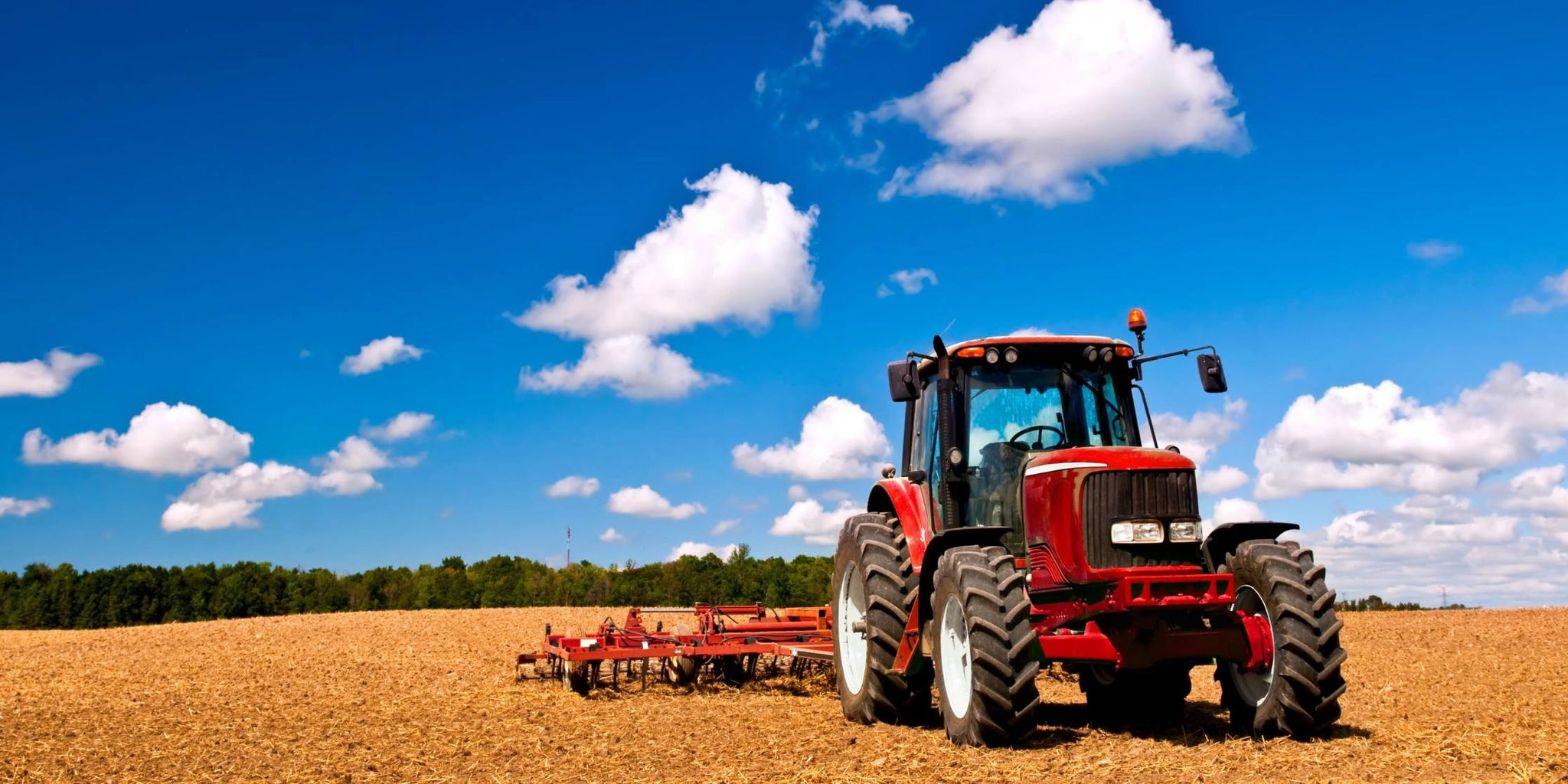 Red tractor in a field with a blue sky and clouds