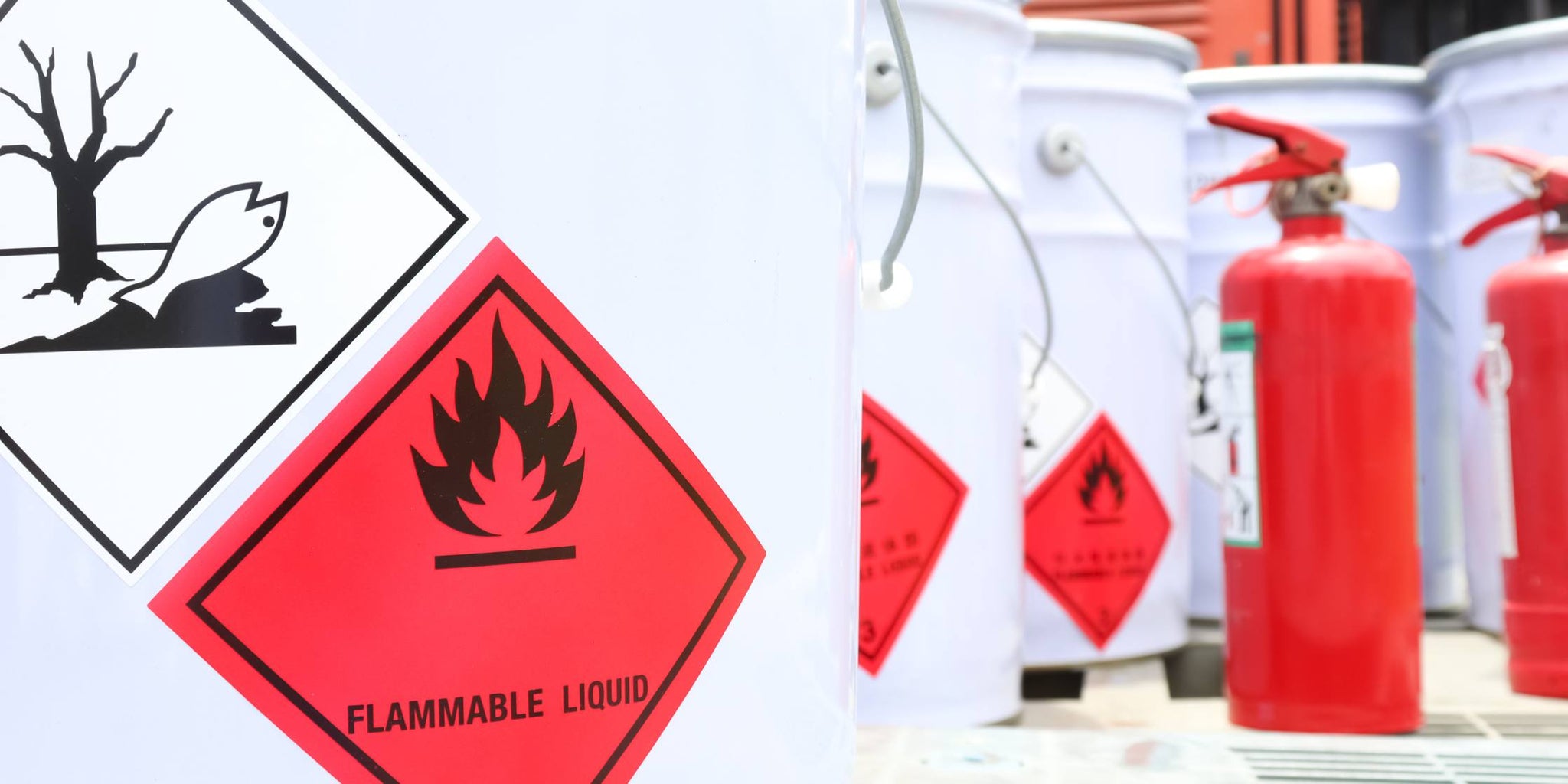 Red Flammable liquid symbol on a white chemical tank in the foreground, red fire extinguishers in the background
