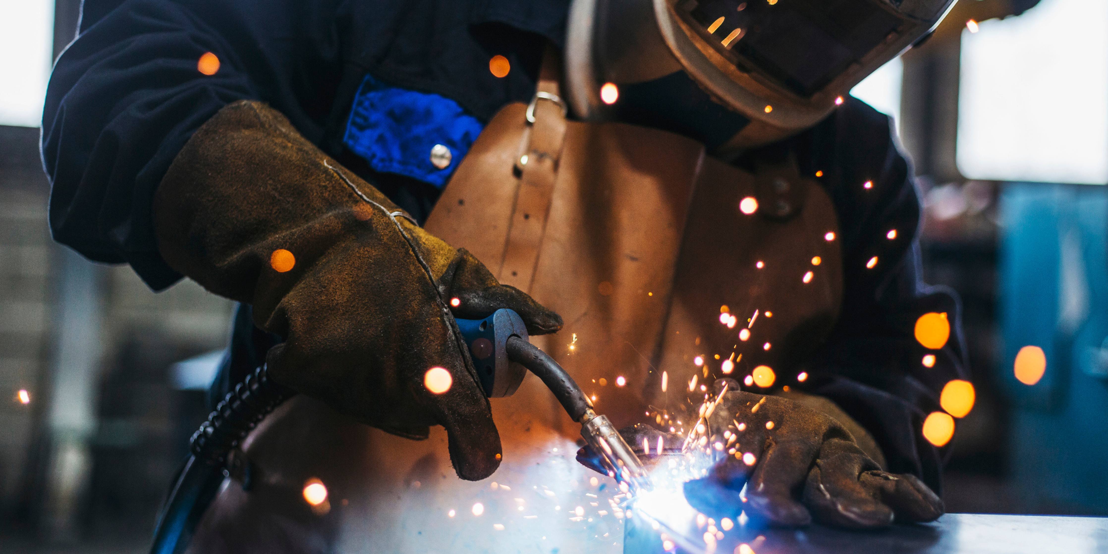 Image of a person welding wearing safety shield, vest and gloves