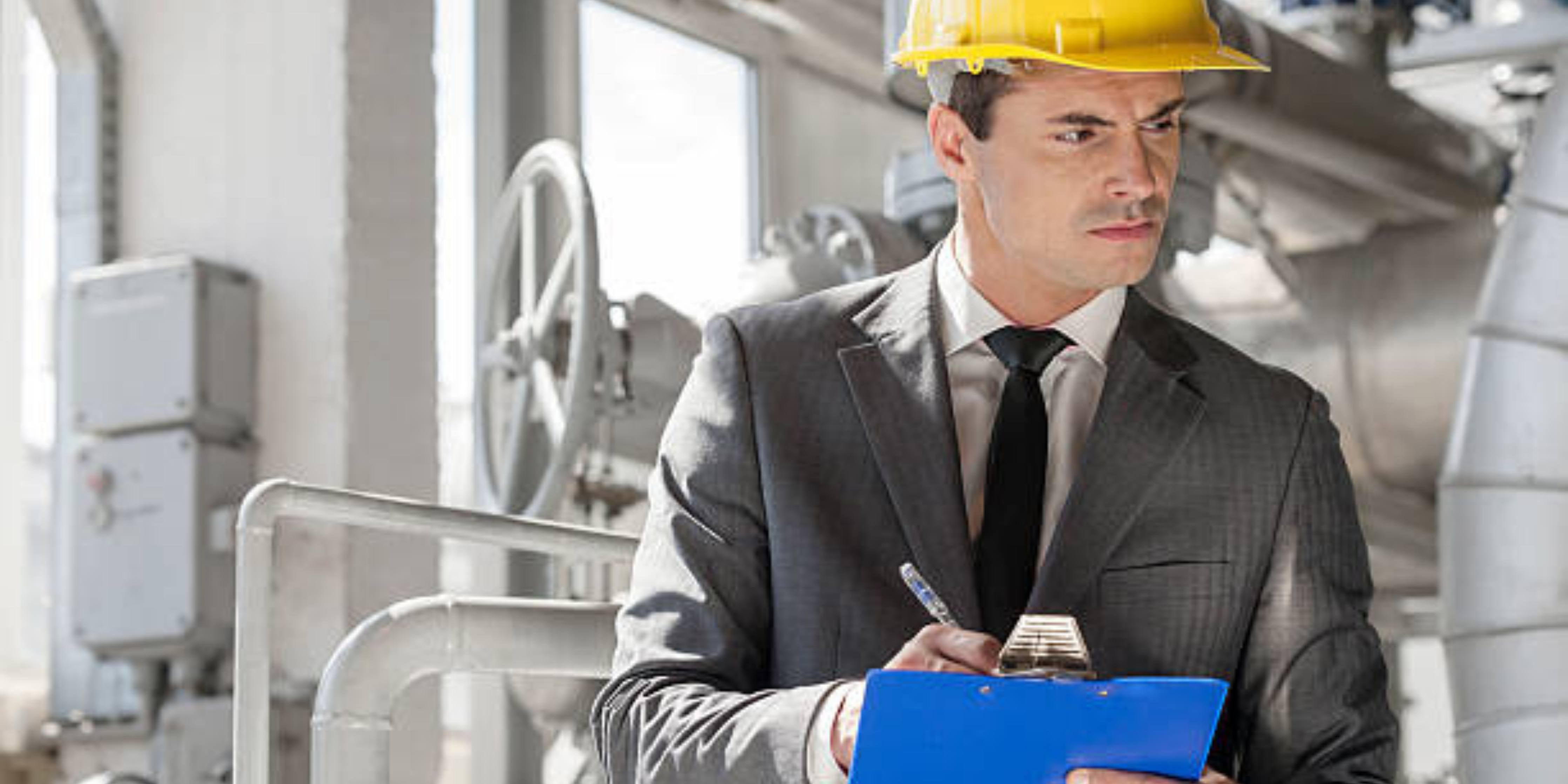 Man holding clipboard with hard hat on, in manufacturing setting for workplace inspections