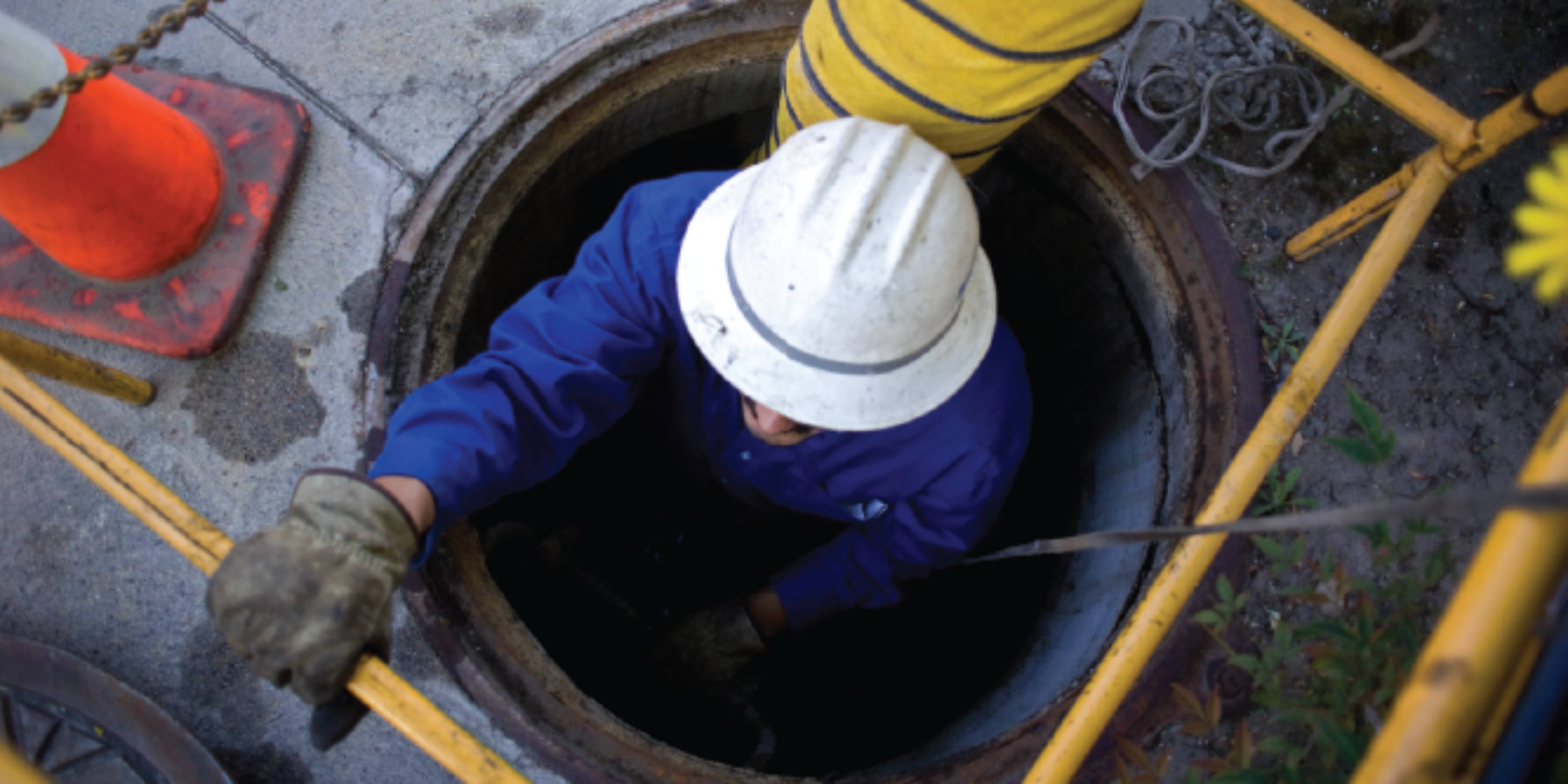 man wearing safety clothing, hard hat and gloves working in a confined space.