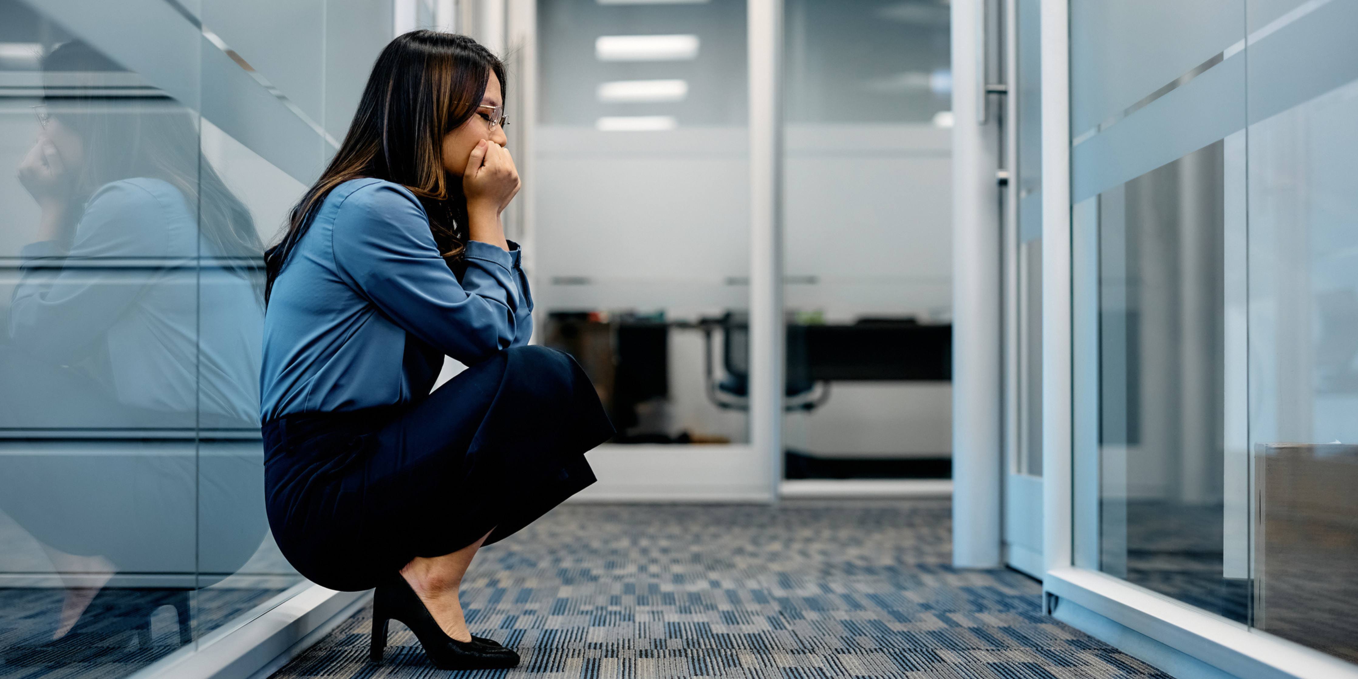 woman crouching on floor in office with hands at face